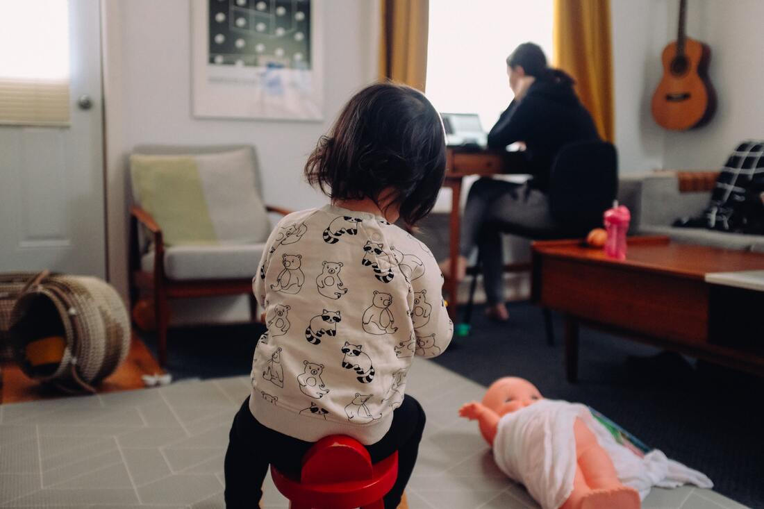 little girl playing in the living room while mom works on laptop