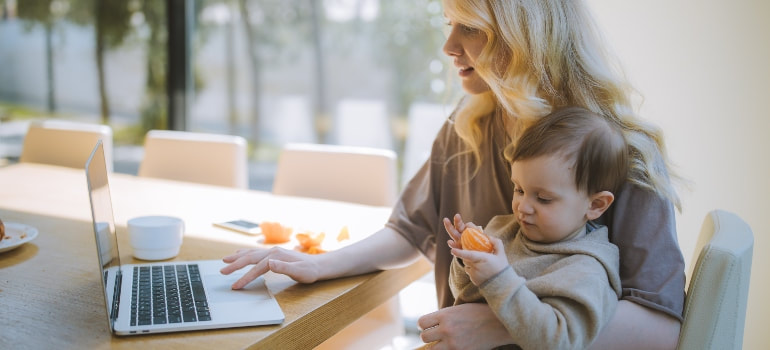 mother holding her baby while working on laptop