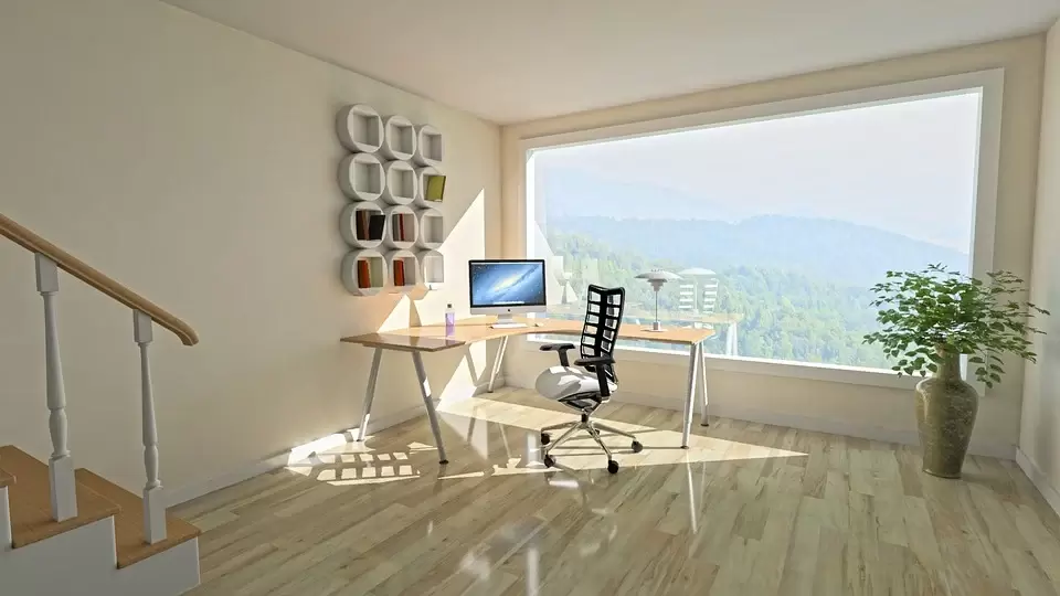 A desk with a monitor and chair placed next to a big window representing an example of a productive home office