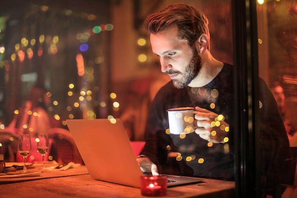 A man holding a mug and looking at his laptop.